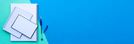 Banner of back to school concept. Stack of white spiral notebook, notepad and notepaper with pen, on a blue and aqua colorful background. School office supplies. Top view, flat layの写真素材