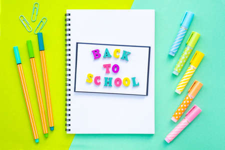 Back to school inscription made of multicolored letters. A stack of notebooks on a spiral overlap. Bright, colorful yellow with mint color background. Markers and markers aroundの写真素材