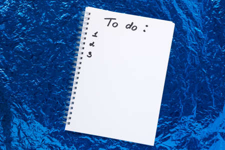 Handwritten inscription to do list in a notebook on spirals and numbers below. Against a background of blue crumpled foil. Concept for New Year, Christmas and new plans for next year.の写真素材