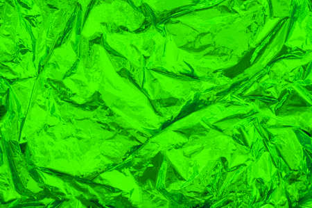 Green crumpled, creased iridescent metal foil texture. Shiny monochrome surface. Abstract colored background.の写真素材