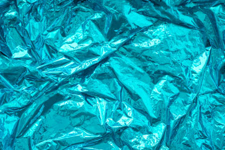 Aqua blue crumpled, creased iridescent metal foil texture. Abstract colored background. Shiny monochrome surface.の写真素材