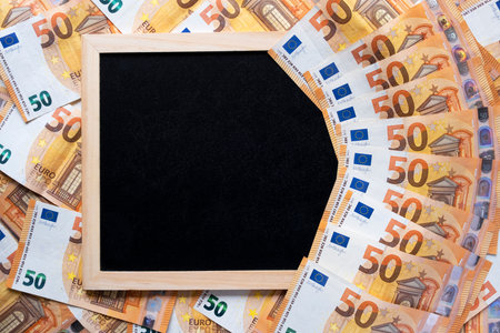 Black clarkboard as a frame on a background of money and a fan of 50 euros from above. Flat lay. Copy space, top view.の写真素材