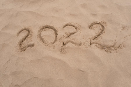 Inscription 2022 on sea or ocean shore. Drawing on sand surface texture. Top view, copy space.の写真素材