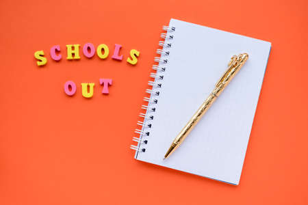 Inscription Schools out from colorful wooden letters. Lie near white blank notepad with gold pen. School end celebration concept. Flat lay, copy space.の写真素材