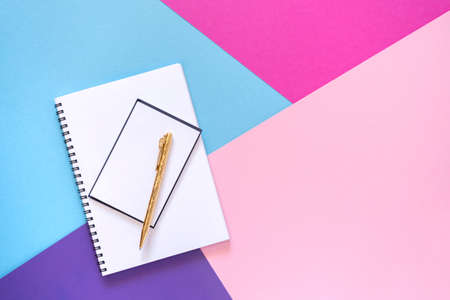 Notebook and gold pen. Purple, pink, and light blue paper background. Geometric figures, shapes, lines. Multicolor abstract flat lay. Copy space, top view. Back to school concept.の写真素材