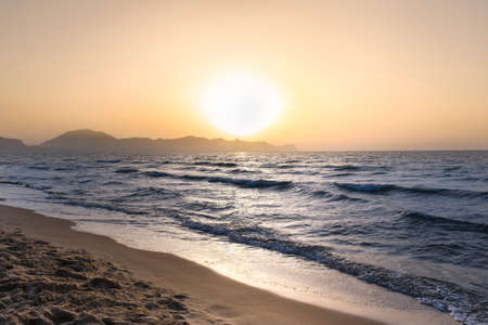 Sun sets behind the mountains in the background. Beautiful orange sunset on the island of Sicily, Italy. Lido lagoa Balestrate beach.の写真素材