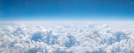Over clouds. Banner with blue sky and white cumulus cloud. Aerial view from airplane window.