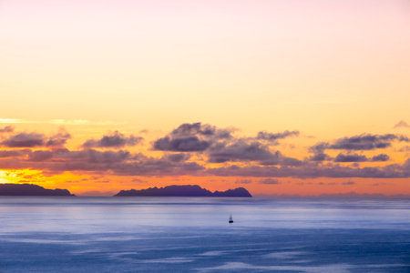 A small sailboat in front of Deserta Island, near Madeira, Portugal. Beautiful sunset over the ocean.の写真素材