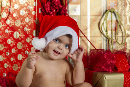 This is a baby with a christmas hat and surrounded by giftsの写真素材
