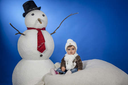 a baby with a hat and scarf next to a snowmanの写真素材