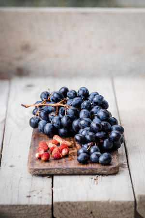 Bunch of ripe blue grapes and wild strawberries on a light wooden background. Fresh autumn fruits. Light food photography.の写真素材