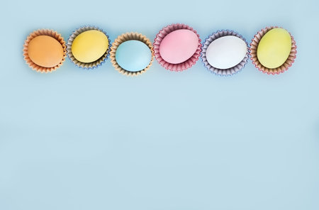 Flat lay row of colorful eggs on a light blue background.  Pastel colors, vintage card. Negative...