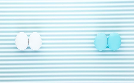 Pair of white and light blue eggs on a colorful striped backdrop. Creative design, minimal concept. Negative spaceの写真素材