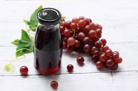 Glass bottle of grape juice with bunch of fresh red grape fruits on wooden background, Summer refreshing drinksの写真素材