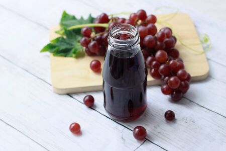 Refreshing drinks with grape juice in glass bottle with bunch of fresh red grapes on wooden table background, Summer drinks, Fresh vitaminsの写真素材
