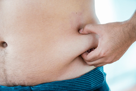 Fat Man holding lumps of fat at the waist of their own to tell herself a weight limit.の写真素材