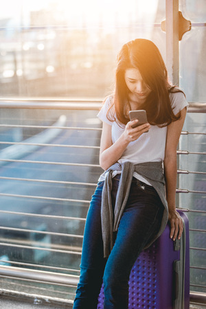 Asian teenage girl is using a smartphone to check flight at the international airport to travel on weekends.の写真素材