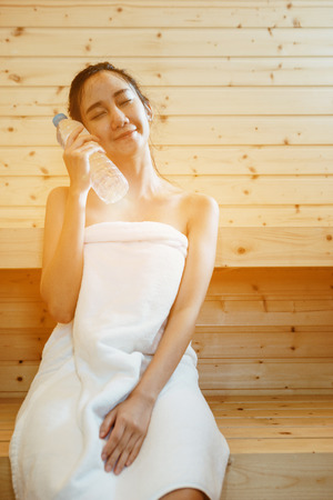 Teen Asian women are sitting in the sauna with holding a drinking water bottle in hand.の写真素材