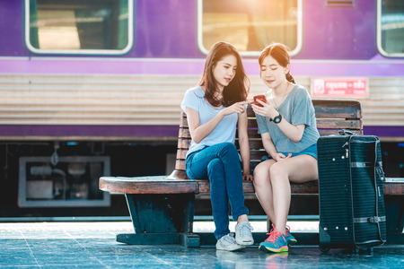 Teen Asian girls use smart-phone for checked baggage train platform area prepared to ready to go outside. Thailand on weekends. From Bangkok to Chiang Maiの写真素材