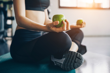 Asian woman exercising in the gym, Young woman workout in fitness for her healthy and office girl lifestyle. She is holding green apple.の写真素材