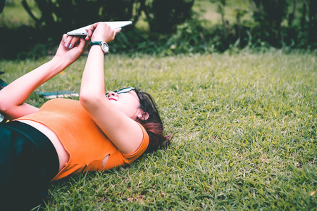 Asian teenage girls sit and relax use tablet to play the Internet to play in the park on weekends.の写真素材