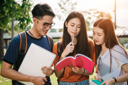 A group of young or teen asian student in university smiling and reading the book and look at the tablet or labtop computer in summer holiday.の写真素材