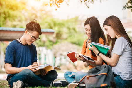 A group of young or teen asian student in university smiling and reading the book and look at the tablet or labtop computer in summer holiday.の写真素材
