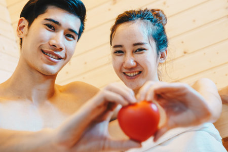 Couple, man and woman were sitting and drinking wine in the sauna, which  installed in their beautiful home. They holding the heart model and close up it.の写真素材