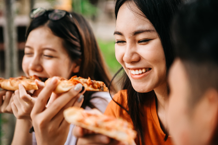 Asian students eating eating the pizza together in breaking time early next study class having fun and enjoy party, Italian food slice with cheese delicious at university outdoor.の写真素材