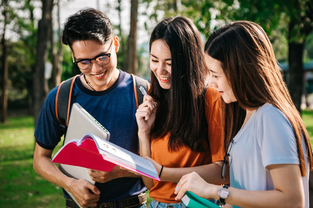 A group of young or teen Asian student in university smiling and reading the book and look at the tablet or laptop computer in summer holiday.