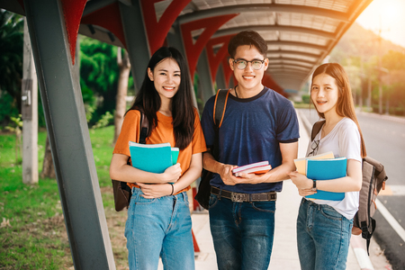 A group of young or teen Asian student in university smiling and reading the book and look at the tablet or laptop computer in summer holiday.の写真素材