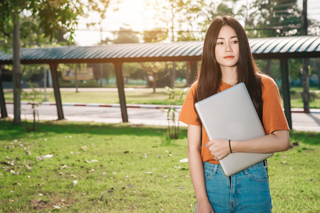 A young or teen asian girl student in university and holding the laptop computer in summer holiday in the park.の写真素材
