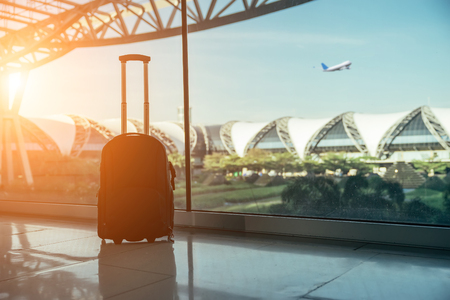 Silhouette of luggage or suitcase placed at the window at waiting terminal in international airports in Thailand with the airplan taking off behide the building.の写真素材