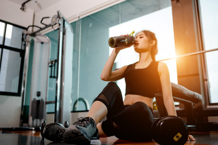 Asian woman exercising in the gym, Young woman workout in fitness for her healthy and office girl lifestyle. she is drinking a protein shake.の写真素材