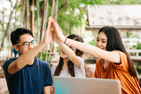 A group of young or teen Asian student in university smiling and reading the book and look at the tablet or laptop computer in summer holiday.の写真素材