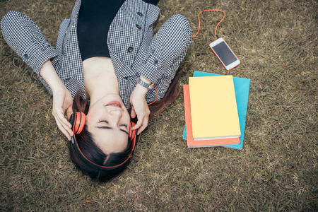 A young teenage student in university smiling and reading the book in summer holiday. She listening the music while reading the book.の写真素材