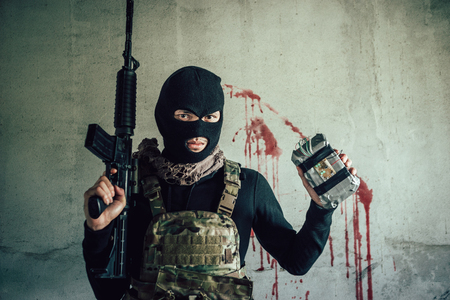 A terrorist wearing a hat to hide his face, he is holding a gun and bomb.の写真素材