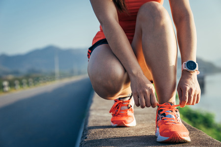 An asian woman athletic is jogging on the concrete road, she is warming her body and tideten her tying her shoes tightly fitting before workout.の写真素材