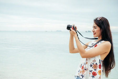 An Asian young woman or girl walking on the beach, she using camera to capture the sky.の写真素材