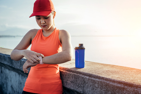 An asian woman athletic is jogging on the concrete road, she is warming her body and tideten her tying her shoes tightly fitting before workout.の写真素材