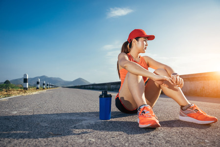 An asian woman athletic is jogging on the concrete road, she is warming her body and tideten her tying her shoes tightly fitting before workout.の写真素材