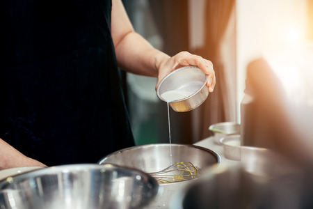 Asian women pouring milk which is an ingredient for making the cake into stainless bowl in her kitchen.の写真素材
