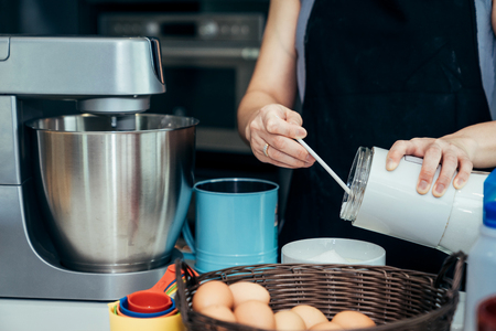 Asian women are mixing the ingredients of a cake in a stainless bowl in her kitchen for weekend party.の写真素材