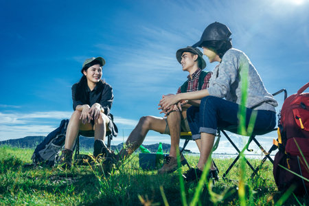 A  group of Asian friends sitting on chairs, drinking some beer and water together outside the tent...