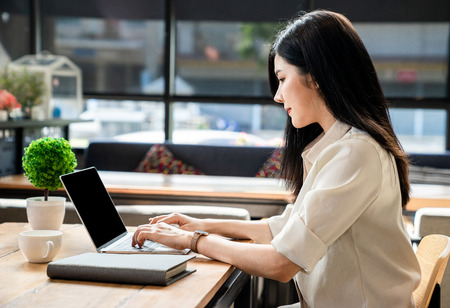 An Asian girl is freelancer woman, she is working by using the laptop computer and drinking a cup of coffee on morning in a coffee shop or her office.の写真素材