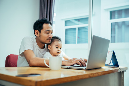 Asian father and his son is using the laptop computer at their home on sunday or holiday.の写真素材