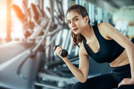 Asian woman exercising in the gym, Young woman workout in fitness for her healthy and office girl lifestyle. She using smart phone to check an email or listening music.の写真素材