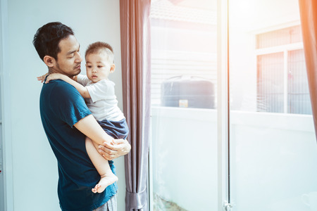 Asian men are father ironing clothes and carrying his son or little boy in their home on holiday.の写真素材