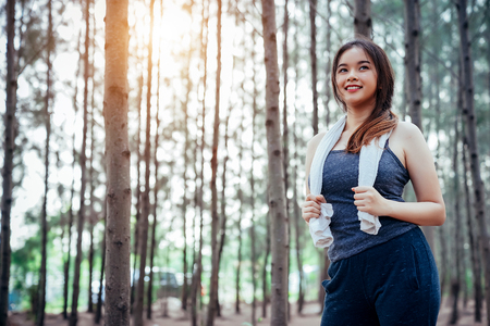 Asian girl is exercising and drinking cool water at the weekend in a pine forest green and lush beautiful. Sport girl and lifestyle concept.の写真素材