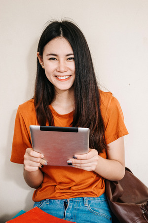A young or teen Asian student in university smiling and reading the book and look at the tablet or laptop computer in summer holiday.の写真素材